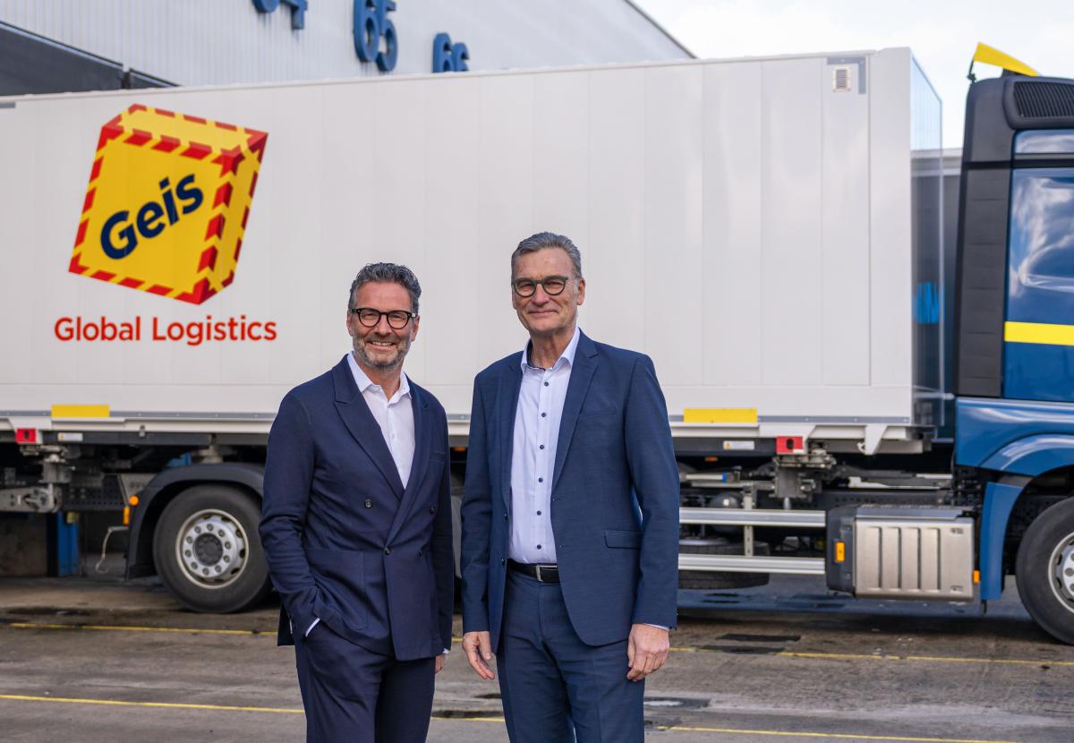 Two men wearing business suits in front of a truck with the logo of the Geis Group